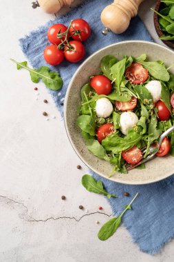 Healthy eating and dieting. Fresh salad with arugula, cherry tomatoes, mozzarella cheese and hard cheese on white wooden background. Top view