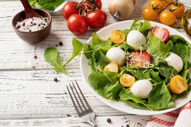 Healthy eating and dieting. Fresh salad with arugula, cherry tomatoes, mozzarella cheese and hard cheese on white wooden background. Top view