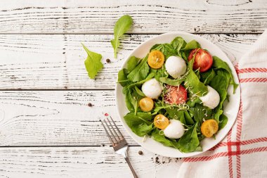 Healthy eating and dieting. Fresh salad with arugula, cherry tomatoes, mozzarella cheese and hard cheese on white wooden background. Top view