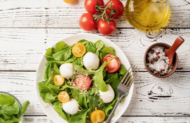 Healthy eating and dieting. Fresh salad with arugula, cherry tomatoes, mozzarella cheese and hard cheese on white wooden background. Top view