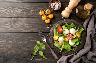 Healthy eating and dieting. Fresh salad with arugula, cherry tomatoes, mozzarella cheese and hard cheese on dark wooden background. Top view