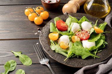 Healthy eating and dieting. Fresh salad with arugula, cherry tomatoes, mozzarella cheese and hard cheese on dark wooden background. Top view