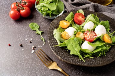 Healthy eating and dieting. Fresh salad with arugula, cherry tomatoes, mozzarella cheese and hard cheese on dark background. Top view