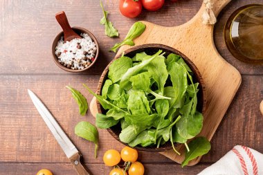 Healthy eating and dieting. Fresh arugula leaves in brown coconut bowl on wooden background top view, flat lay