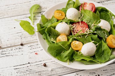 Healthy eating and dieting. Fresh salad with arugula, cherry tomatoes, mozzarella cheese and hard cheese on white wooden background. Top view