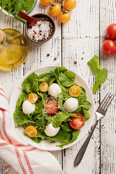 Healthy eating and dieting. Fresh salad with arugula, cherry tomatoes, mozzarella cheese and hard cheese on white wooden background. Top view