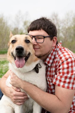 Summer leisure time, pet care and training. Happy man plays with mixed breed shepherd dog on green grass