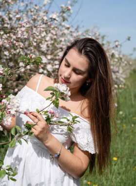 Spring concept. Nature. Young caucasian woman in white summer dress enjoying the flowering of an apple trees, walking in spring apple gardens