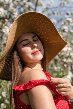 Spring concept. Nature.Young caucasian woman in red dress and summer hat enjoying the flowering of an apple trees, walking in spring apple gardens