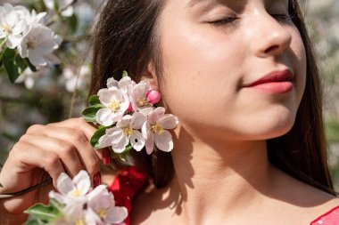 Spring concept. Nature.Young caucasian woman in red dress and summer hat enjoying the flowering of an apple trees, walking in spring apple gardens