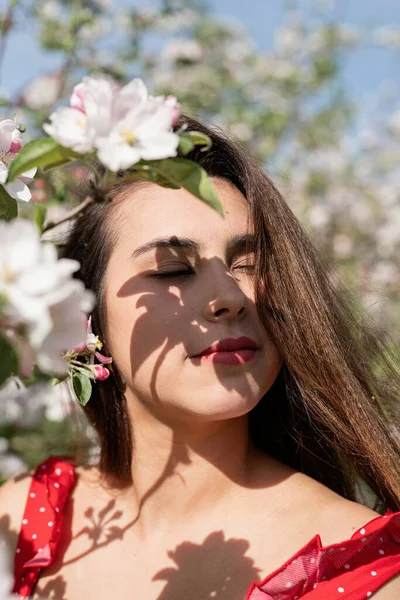 Spring concept. Nature.Young caucasian woman in red dress and summer hat enjoying the flowering of an apple trees, walking in spring apple gardens