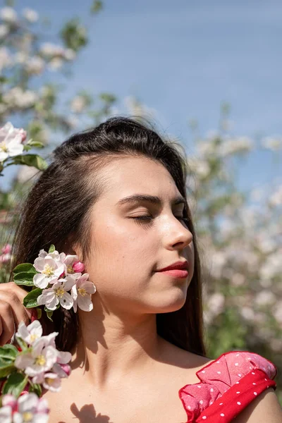 Spring concept. Nature.Young caucasian woman in red dress and summer hat enjoying the flowering of an apple trees, walking in spring apple gardens