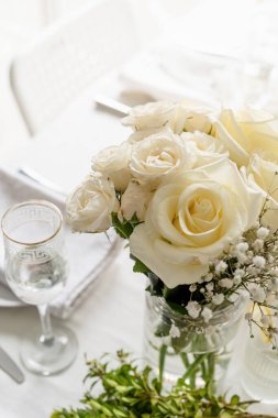 Wedding table set up in taditional style with roses grass and greenery. Close up of white roses bouquet