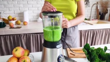front view of woman making healthy smoothie with blender at the kitchen