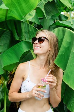 Summer vacation. Beautiful woman in white swimsuit with long hair and palm leaves. Beautiful caucasian girl in stylish swimwear in tropical nature