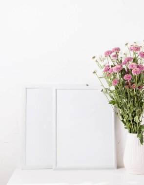 White frame mockup with chrysanthemum flowers in a vase on a white table, mockup design