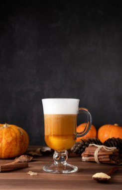Autumn hot drinks. Pumpkin spice latte in a glass mug with cinnamon and ginger on dark background with copy space