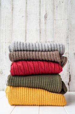 Hello fall. Cozy warm image. Stack of autumn warm sweaters on white wooden background