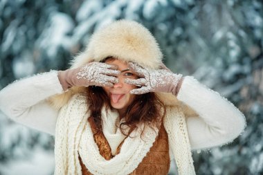 Kazaklı ve kışın eldivenli bir kadın gözlerini gizliyor ve karlı bir ormanda bir popo gösteriyor. Komik kadın portresi.