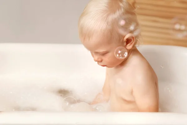 Baby sitting in the bath and looking at the water. — Stock Photo, Image