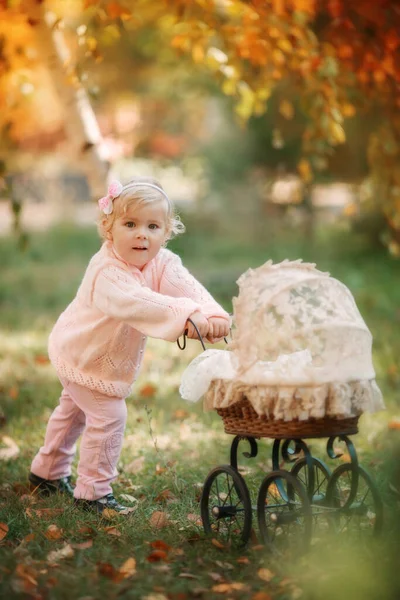 Linda menina loira ao ar livre ficando perto de carrinho de bebê para bonecas e sorrindo. — Fotografia de Stock