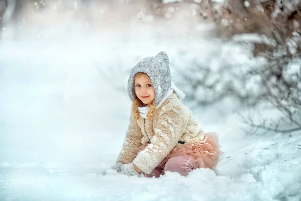 Küçük kız karlı kış gününde parkta oynuyor..