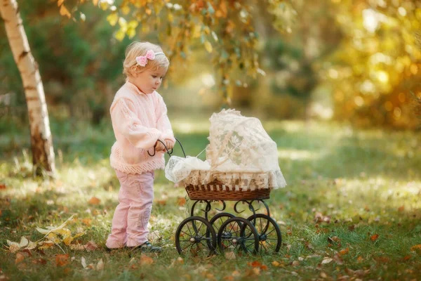 Krásná blond holčička venkovní pobyt v blízkosti baby kočárek pro panenky a usmívá. — Stock fotografie