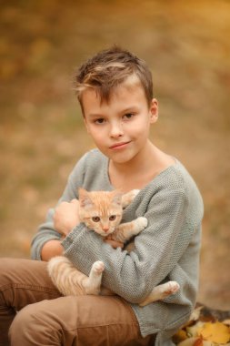  Sonbahar bahçesinde kırmızı kedili bir çocuk.