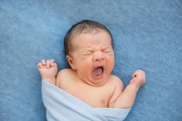  Battaniyeyle kaplanmış mavi arka planda yeni doğmuş bir bebek.