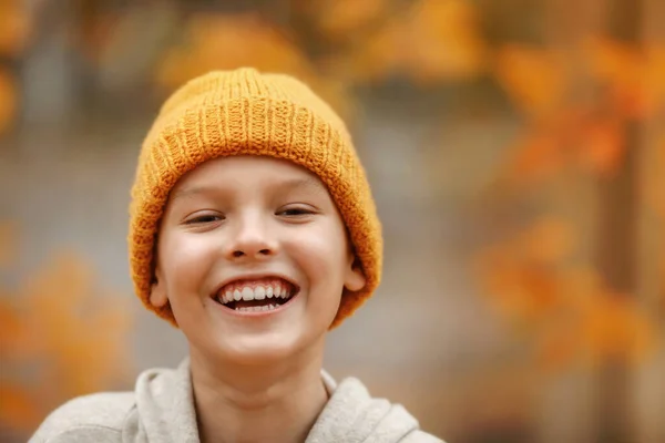Sonbahar parkında şapkalı çocuk gülümsüyor..