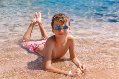 Çocuk denizin kenarındaki kumda yatıyor..