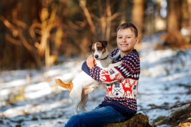 Gün batımında ormanda Jack Russell Terrier 'ın köpeği olan bir çocuk. En iyi iki arkadaş portresi. Çocuk ve köpek ağaç kütüğünde oturuyor.