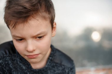 Üzgün çocuk çatık kaşlı duvarın yanında oturuyor. Çocuk çok düşünceli.