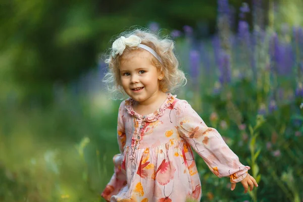 一个穿着紫色花朵的漂亮金发姑娘的画像 卷发小子笑着看着摄像机 — 图库照片