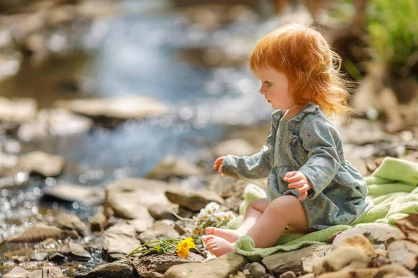 かわいい女の子は ストリーム テキストのためのスペースの近くに座っている 赤い髪の赤ちゃんは自然の中で時間を費やしている — ストック写真