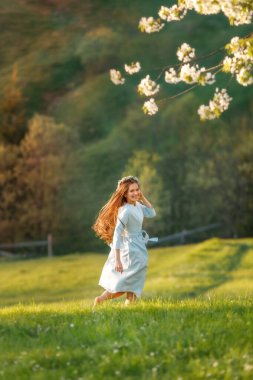 Mavi elbiseli, uzun saçlı güzel bir kadının tam boy portresi. Baharda yeşil tepelerde koşuşturup duruyor.. 