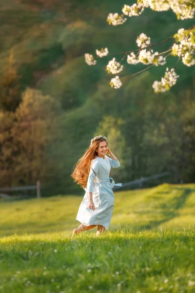 Mavi elbiseli, uzun saçlı güzel bir kadının tam boy portresi. Baharda yeşil tepelerde koşuşturup duruyor.. 