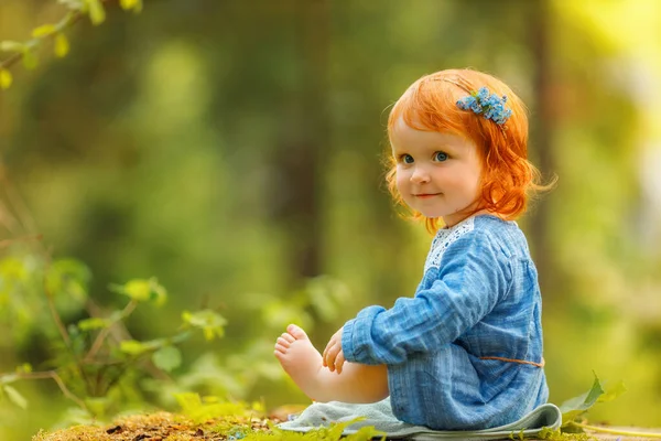 身穿蓝色衣服的红头发女婴坐在公园的大树桩上 在日落时看着看不见的东西 幻想概念 — 图库照片