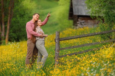 Genç ve sevgi dolu bir çift, ahşap evin arka planında nazikçe sarılıyor. Etrafta bir sürü sarı çiçek dolaşıyor. Birlikte eğleniyoruz.. 