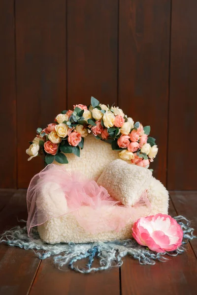 Shoot set up with sofa and a lot of flowers and green wool blanket on the wood background. Photo zone for a photo session of newborns. Setup ready for newborn photo shoot and baby photography.