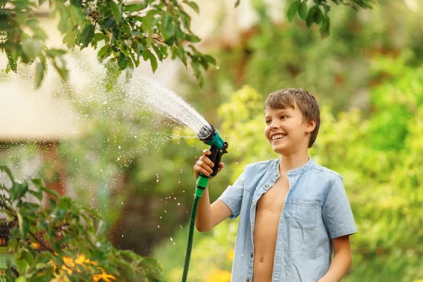 Boy watering flower in garden. Kid with pours water from a hose on summer day. 
