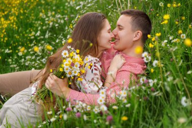 Romantic couple of young people are lying down on grass in field of spring flowers. Woman lies on the man's chest and looks happily. 