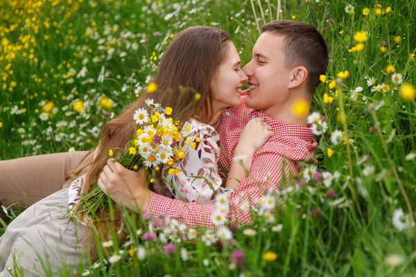 Romantic couple of young people are lying down on grass in field of spring flowers. Woman lies on the man's chest and looks happily. 