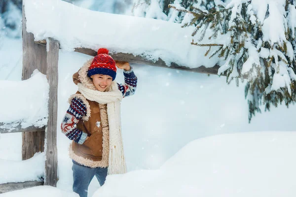 Happy child boy on a winter walk outdoors smiling and looking at camera. Kid is wearing red hat and white scarf. Kid is having fun, playing at winter walk outdoors.