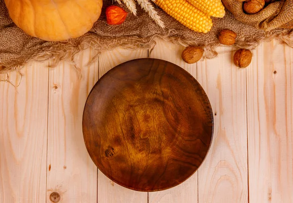 Autumn Thanksgiving table setting. Brown plate on wooden table with pumpkins and autumn decor close up, Thanksgiving holiday menu concept. Vegetables and nuts are on the top of photo.