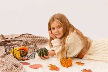 Beyaz kazaklı sarışın kız şükran günü sembollü balkabağı tutuyor. Battaniye ve yerde küçük bir balkabağı. Kidis yerde yatıyor.