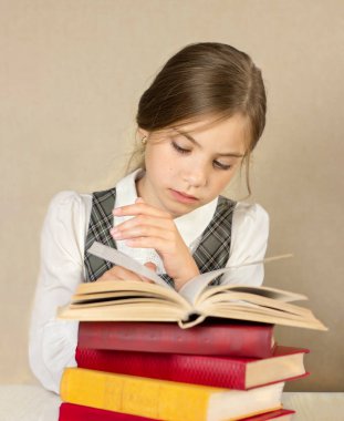 Liseli kız bir yığın kitapla bir masada oturuyor ve yakın plan kitap okuyor.