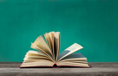 Yeşil arka planda, ahşap bir yüzeye yakın uçan sayfaları olan açık bir kitap.