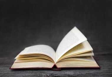 Açık eski bir kitap, gri bir arka planda, koyu ahşap bir yüzeyde yatıyor.