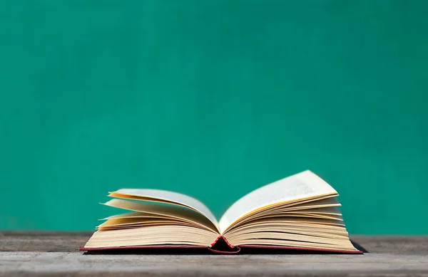 Açık bir kitap, turkuaz bir arka planda gri tahta bir masada yatıyor.